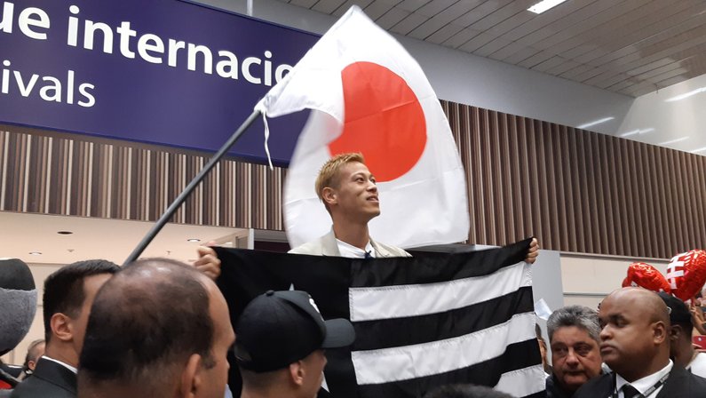 Honda é recepcionado pela torcida do Botafogo no aeroporto do Rio de Janeiro com bandeira do Japão ao fundo
